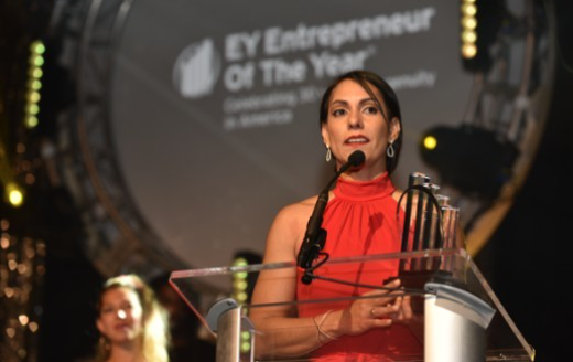 Gaby Isturiz standing at a podium giving a speech while being awarded the "EY Entrepreneur of the Year" award