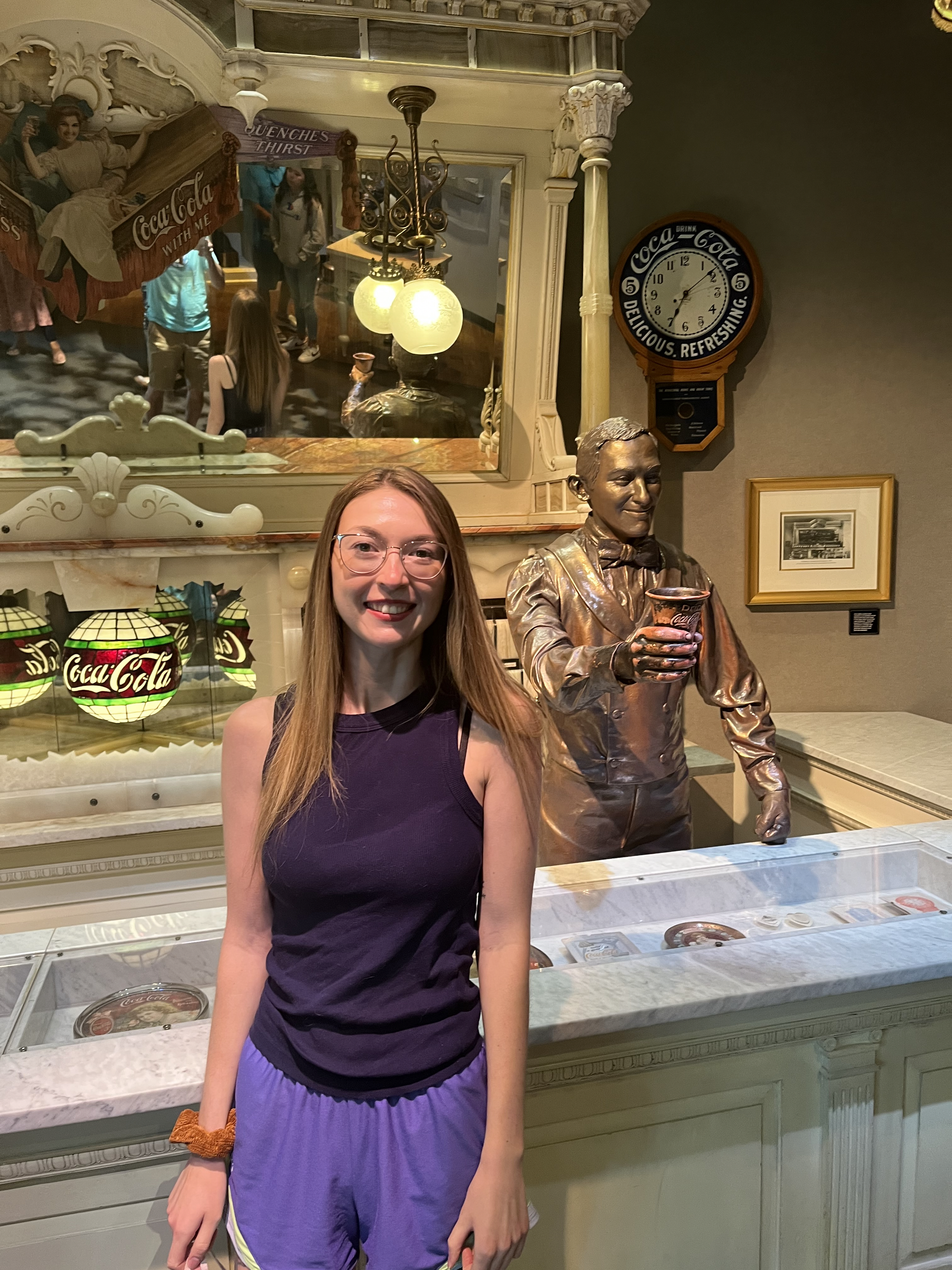 Tiffany smiling in front of a retro soda fountain with a statue of the founder of Coca-Cola, John Pemberton
